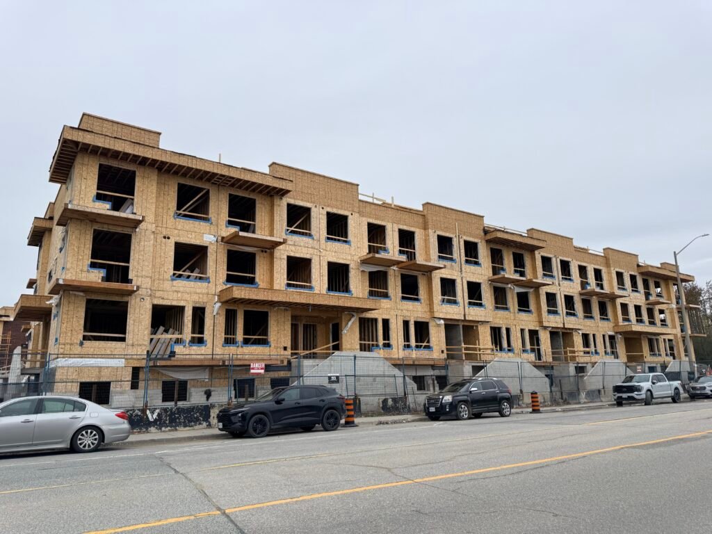 A GTA buyer reviewing new construction purchase documents at a table with a new home development visible through the window