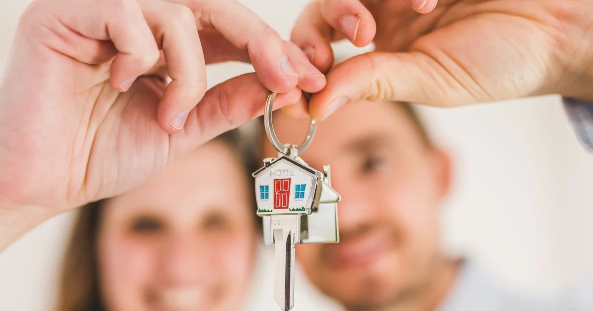 Couple holding house-shaped keychain after buying their first home